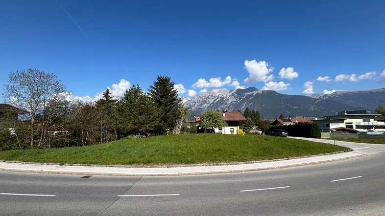 Weitläufige Aufnahme eines Kreisverkehrs mit Grünfläche und Bergblick im Hintergrund unter blauem Himmel.