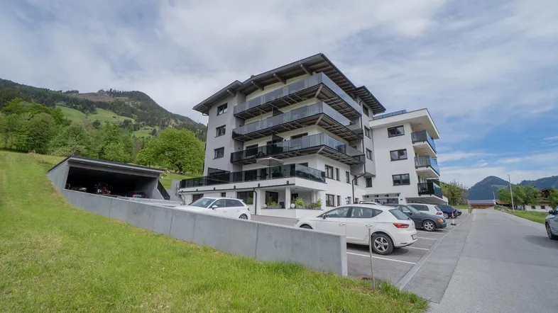 Modernes Apartmentgebäude mit Balkonen und Tiefgaragenzufahrt in alpiner Umgebung.