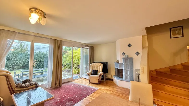Helles Wohnzimmer mit Holzboden, Kamin und direktem Zugang zum Gartenbereich durch große Fenster.