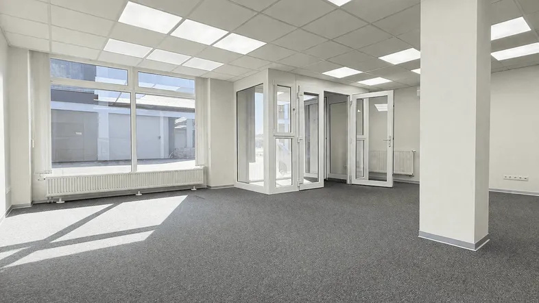 Geräumiges, leeres Büro mit großen Fenstern, Teppichboden und Säulen, bereit zur individuellen Gestaltung.