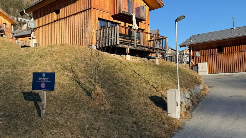 Modernes Holzhaus in alpiner Umgebung mit sonnigem Hanggrundstück und klarem Himmel.