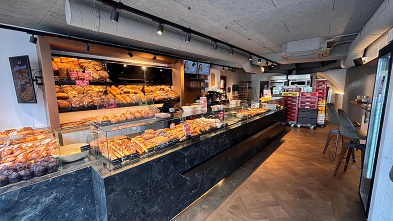 Geräumiger Bäckereiverkaufsraum mit langen Theken, vielen Backwaren und Holzparkettboden im Fischgrätmuster.