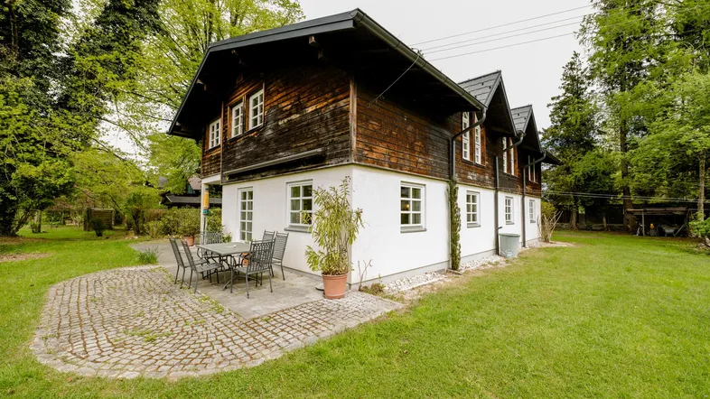 Traditionelles Haus mit Holzfassade und weißem Putz, umgeben von einem grünen Garten mit Terrasse.