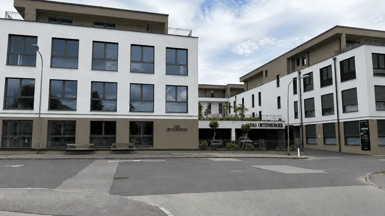 Moderne Wohngebäude mit weißer und beiger Fassade und großen Fenstern unter bewölktem Himmel.