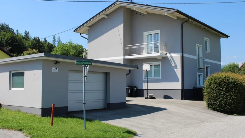 Graues Einfamilienhaus mit Garage und gepflasterter Auffahrt unter blauem Himmel.