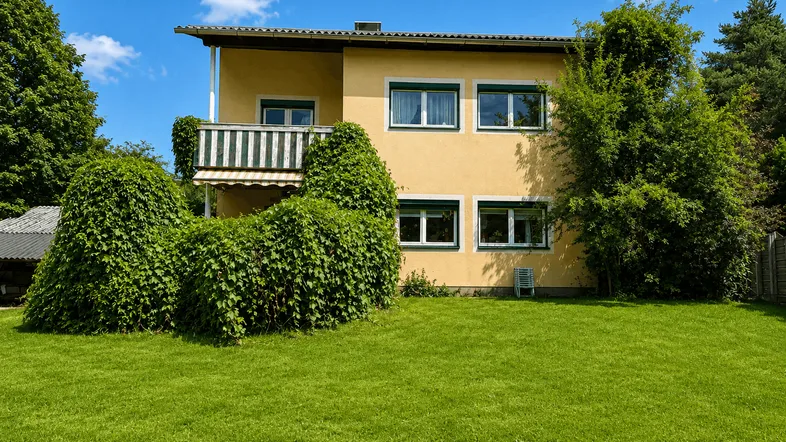 Gelbes Einfamilienhaus mit grünem Rasen und üppiger Bepflanzung unter blauem Himmel.