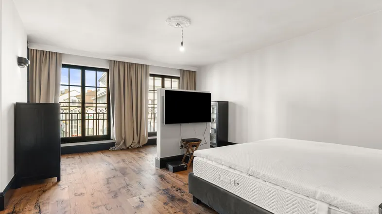 Helles Schlafzimmer mit Holzboden, großen Fenstern und Blick auf die umliegenden Gebäude.
