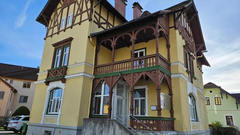 Gelbe Villa mit Fachwerkdetails und Holzbalkonen unter blauem Himmel.