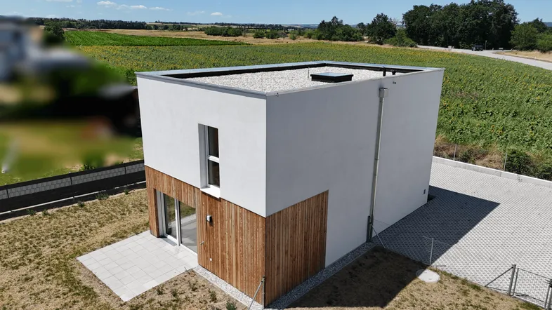 Modernes Einfamilienhaus mit Flachdach und Holzverkleidung, umgeben von Feldern unter blauem Himmel.