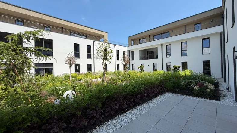 Moderner Innenhof mit gepflegtem Garten, Bäumen und Sträuchern zwischen Wohngebäuden.