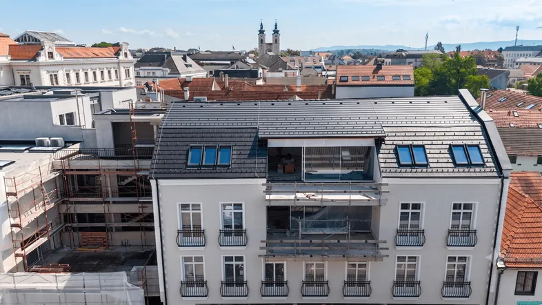 Draufsicht auf ein im Bau befindliches Gebäude mit moderner Dachkonstruktion und städtischer Umgebung.