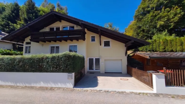 Hausfassade mit Garage, Einfahrt und gepflegter Hecke unter blauem Himmel.