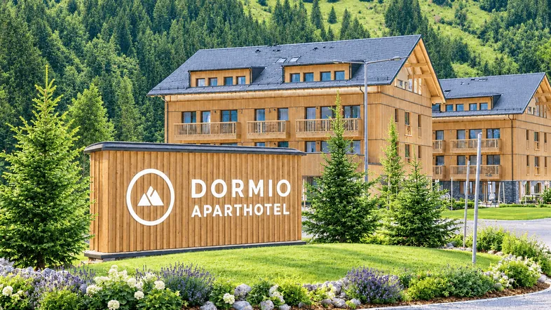 Modernes Aparthotel in Holzbauweise mit gepflegter Grünanlage und Bergkulisse im Hintergrund.