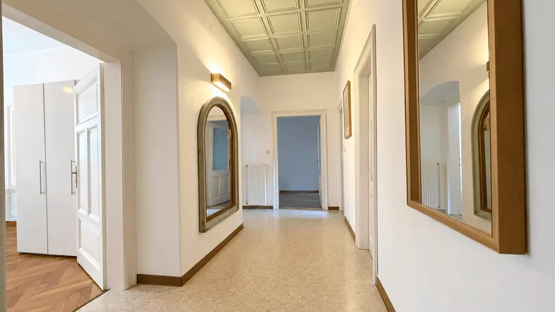 Heller Flur mit Terrazzoboden, dekorativer Decke und Spiegeln, der zu weiteren Räumen führt.