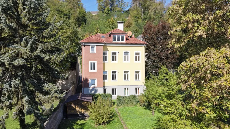 Luftaufnahme eines gepflegten Mehrfamilienhauses mit gelber und roter Fassade, umgeben von Bäumen und Garten.