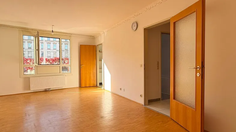 Heller, leerer Wohnraum mit Parkettboden, Stuckdecke und Blick auf die Stadt.