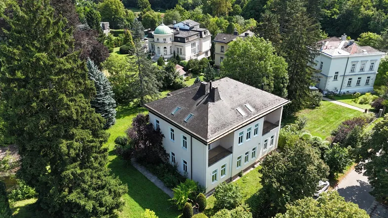 Luftaufnahme einer eleganten Villa umgeben von altem Baumbestand und weiteren historischen Gebäuden.