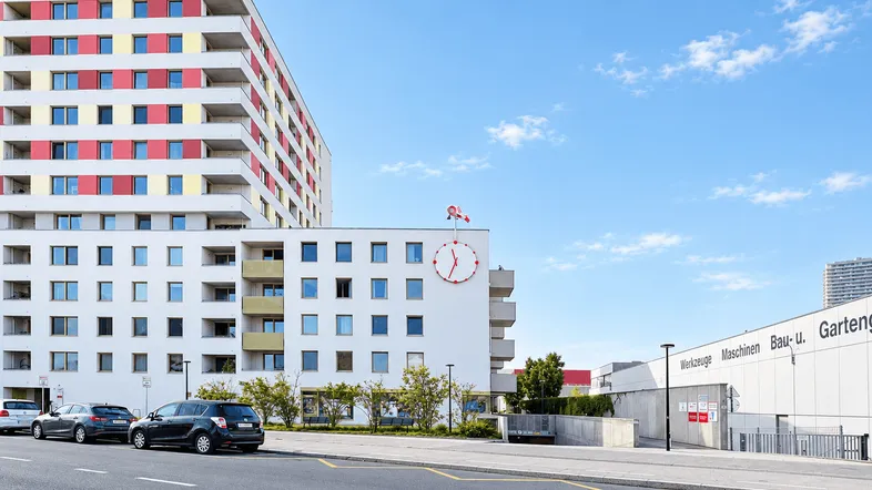 Modernes Wohngebäude mit farbigen Balkonen und einer belebten Straße im Vordergrund unter blauem Himmel.