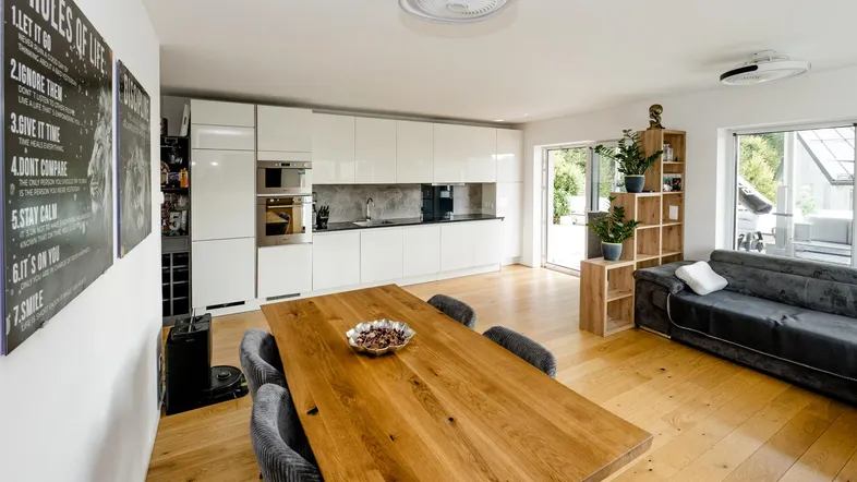 Moderner offener Wohn-Essbereich mit integrierter Küche, Holzboden und Zugang zur Terrasse.
