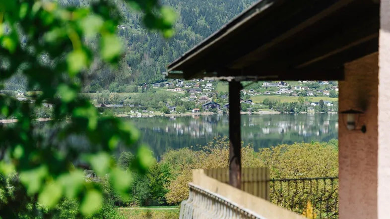 Blick von einem Balkon auf einen See, umgeben von grünen Hügeln und einem Dorf.