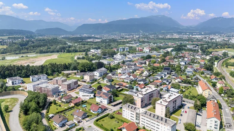 Luftaufnahme einer Wohnsiedlung mit Bergen im Hintergrund und einem Fluss in der Ferne.