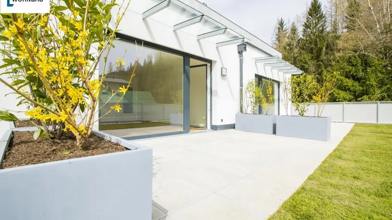 Moderne Terrasse mit großen Schiebetüren, Pflanzenkübeln und angrenzender Rasenfläche.