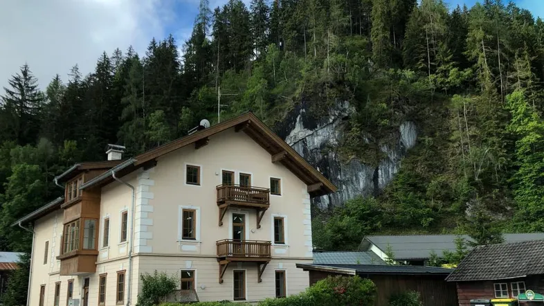 Traditionelles Gebäude mit Holzbalkonen und einem bewaldeten Berghang im Hintergrund.