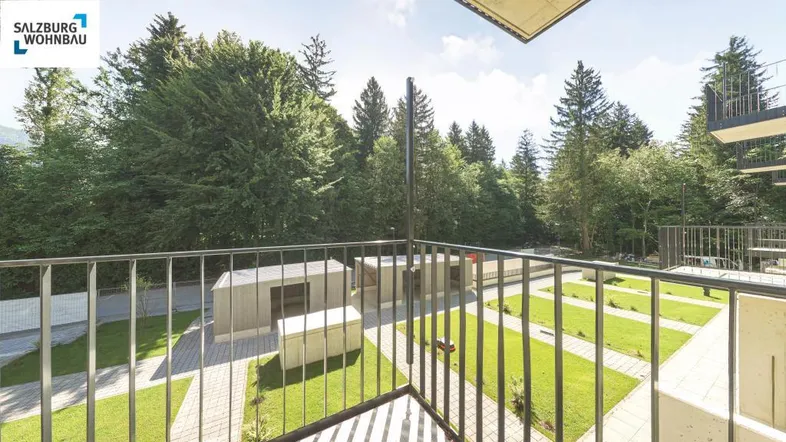 Blick vom Balkon auf die gepflegte Grünanlage mit Bäumen und Sitzgelegenheiten im Freien.