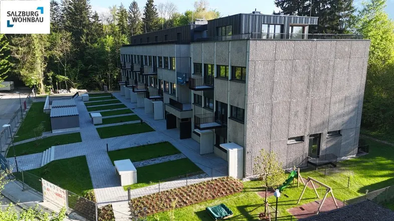 Modernes Mehrfamilienhaus mit gepflegten Grünflächen, Gehwegen und einem kleinen Spielplatz.