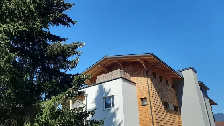 Modernes Gebäude mit Holzfassade und markantem Dachüberstand unter blauem Himmel.