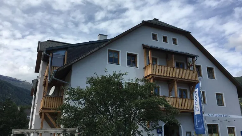 Mehrfamilienhaus mit traditioneller Architektur, Holzbalkonen und einem kleinen Spielplatz im Vordergrund.