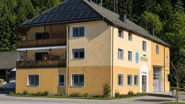 Mehrfamilienhaus mit Photovoltaikanlage, Balkonen und Blick auf die umliegende Berglandschaft.