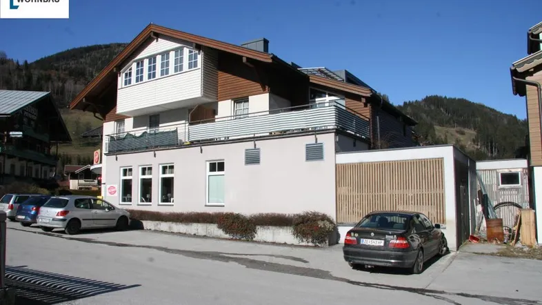 Mehrstöckiges Gebäude mit Balkonen und Parkplätzen, eingebettet in eine malerische Berglandschaft.
