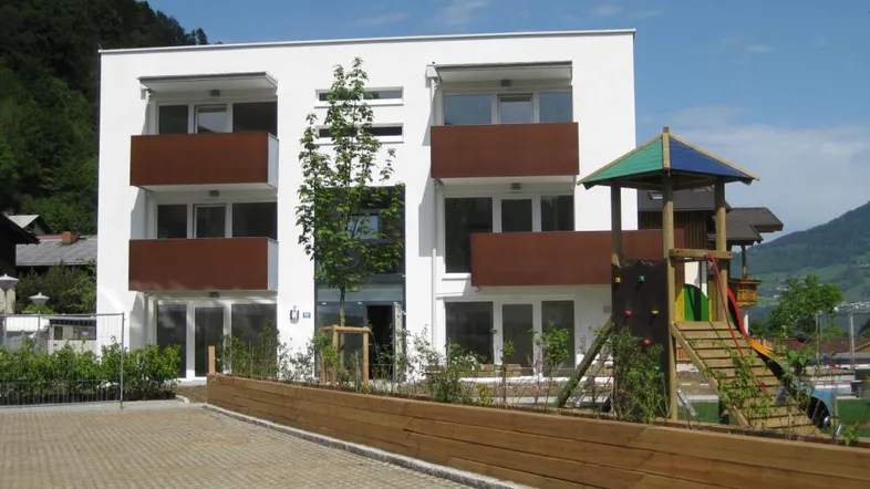 Modernes Wohngebäude mit weißen Fassaden, braunen Balkonen und einem Kinderspielplatz im Vordergrund.