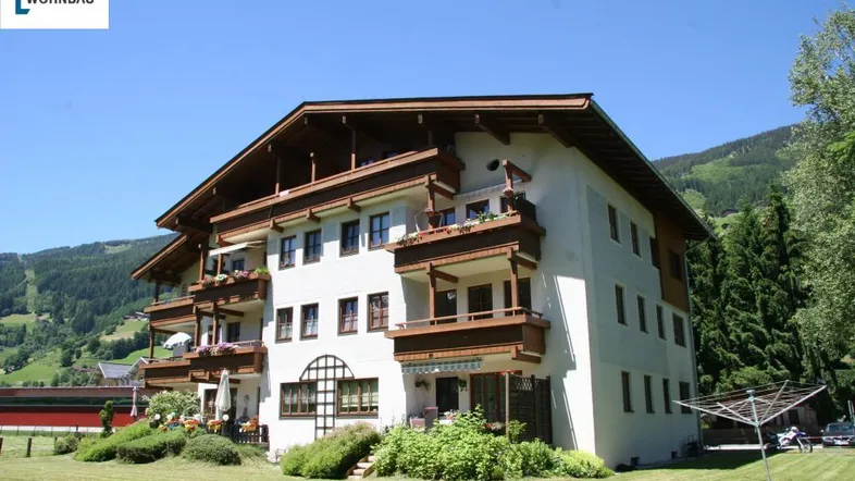 Mehrfamilienhaus im alpinen Stil mit Balkonen und Garten in einer malerischen Berglandschaft.