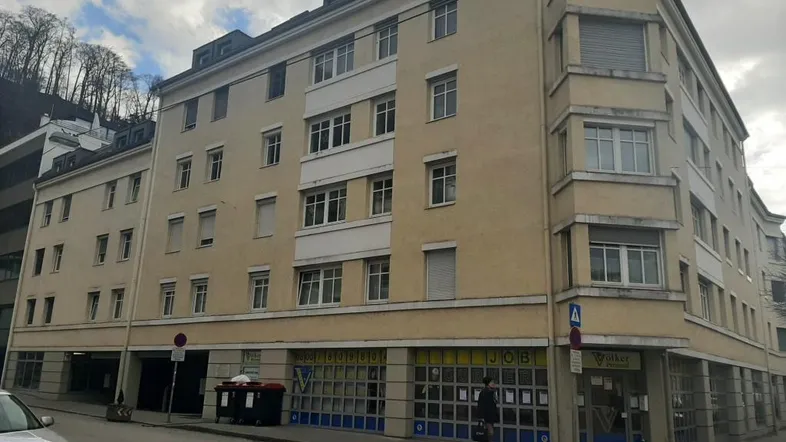 Mehrstöckiges Wohn- und Geschäftshaus in städtischer Umgebung mit Rollläden an den Fenstern.