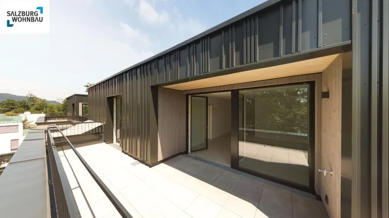 Moderne Dachterrasse mit Fliesenboden und Zugang zu einem hellen Wohnbereich, umgeben von einer Metallfassade.