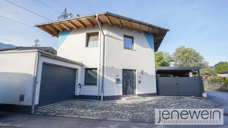 Modernes Einfamilienhaus mit Garage, Carport und gepflastertem Vorplatz unter blauem Himmel.