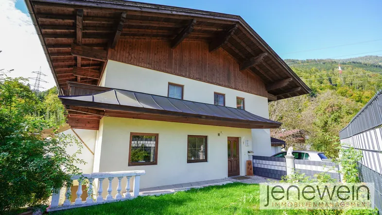 Traditionelles Haus mit Holzelementen und gepflegtem Vorgarten in bergiger Umgebung.