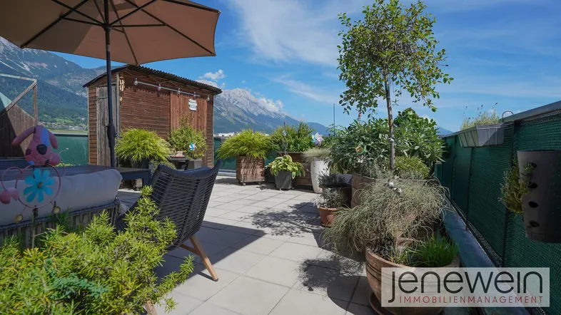 Große Dachterrasse mit Pflanzen, Sitzgelegenheiten und Bergblick unter blauem Himmel.