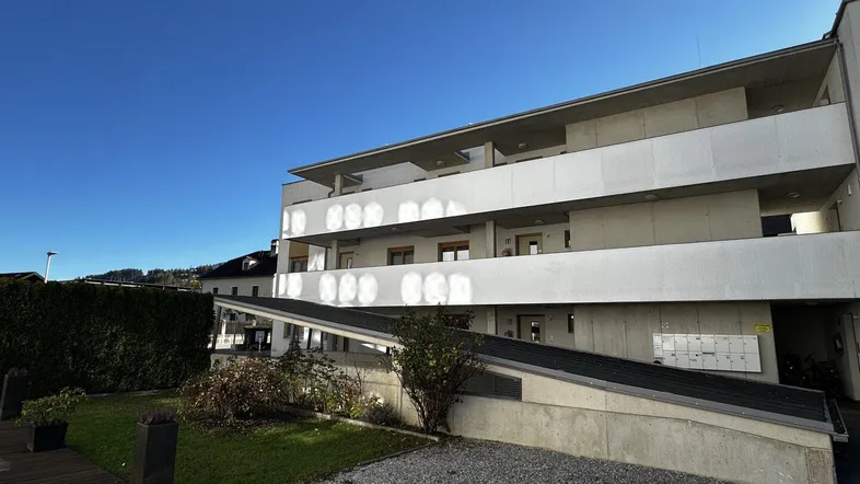 Modernes Mehrfamilienhaus mit Balkonen und gepflegter Außenanlage unter blauem Himmel.