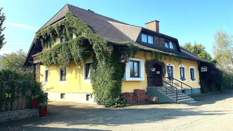 Traditionelles gelbes Gebäude mit üppigem Efeu bewachsen und einem Satteldach unter blauem Himmel.