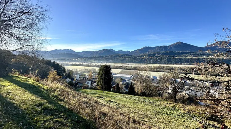 Weitläufiger Blick über ein Tal mit Bergen, Fluss und ländlicher Bebauung unter blauem Himmel.