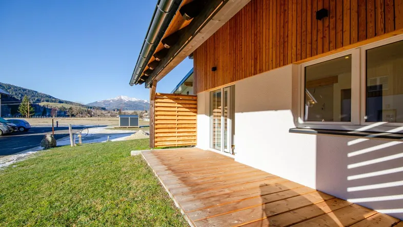 Holzterrasse am Haus mit Blick auf die umliegende Landschaft und Berge unter blauem Himmel.