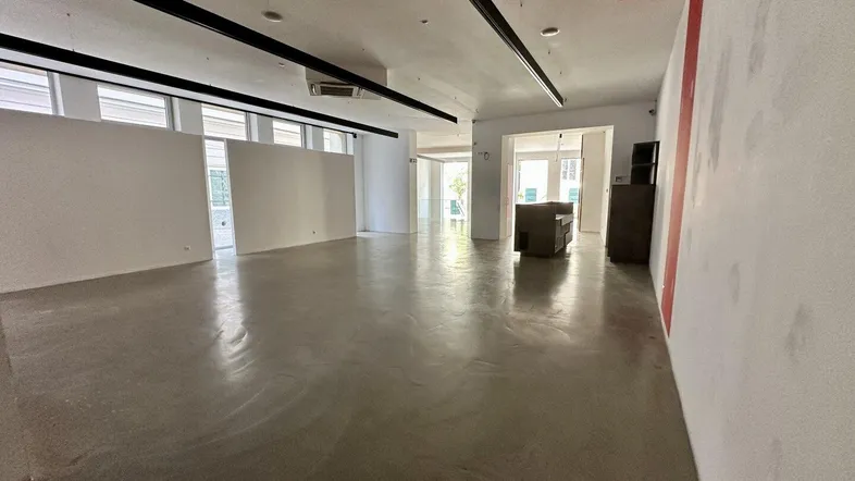 Geräumiger, leerer Geschäftsraum mit hellen Wänden, Betonboden und modernen Deckenleuchten.