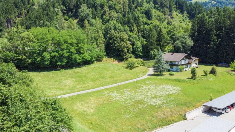 Luftaufnahme eines Hauses mit großem Grundstück, umgeben von Wald und Bergen.