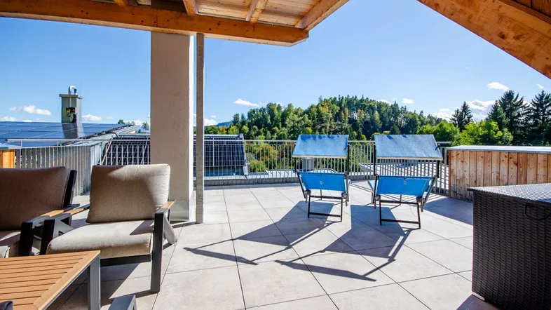 Große Dachterrasse mit Holzdecke, Fliesenboden und bequemen Gartenmöbeln, bietet einen weiten Blick ins Grüne.