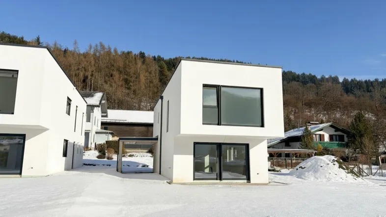 Moderne weiße Architektur in verschneiter Landschaft mit klarem Himmel und Wald im Hintergrund.