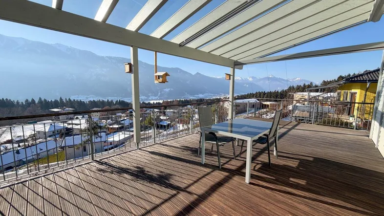 Geräumige Terrasse mit Holzboden, Esstisch und atemberaubendem Bergblick, teilweise überdacht.