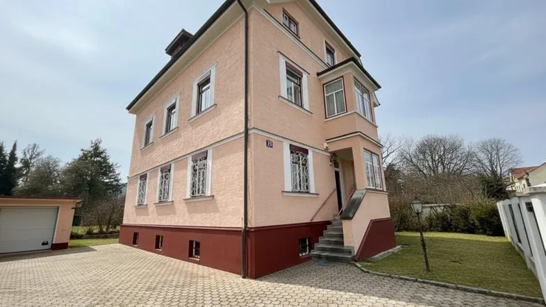 Rosa gestrichenes Mehrfamilienhaus mit gepflasterter Auffahrt und kleinem Vorgarten unter blauem Himmel.